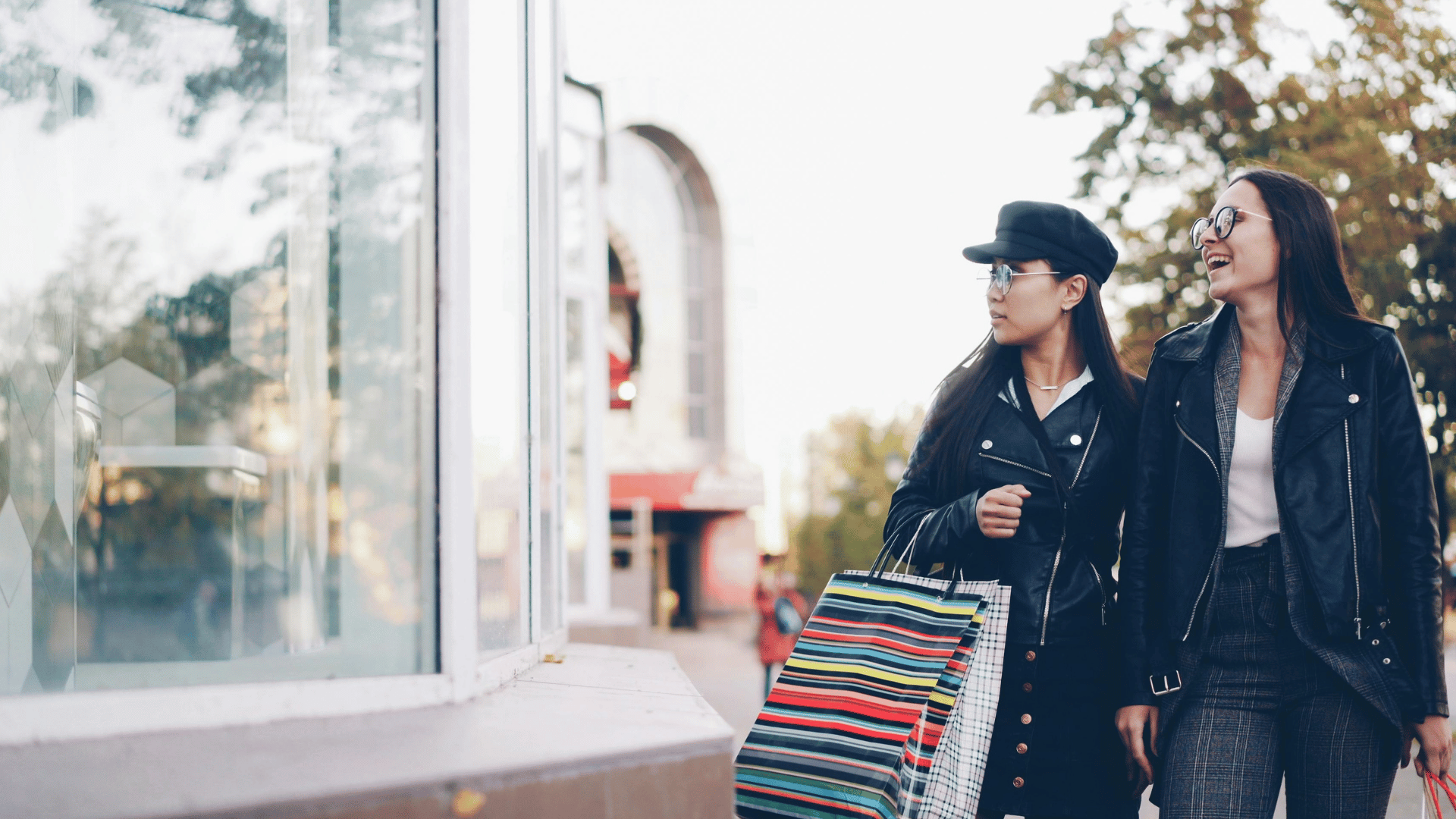 Two women window shopping outdoors with colorful striped shopping bags