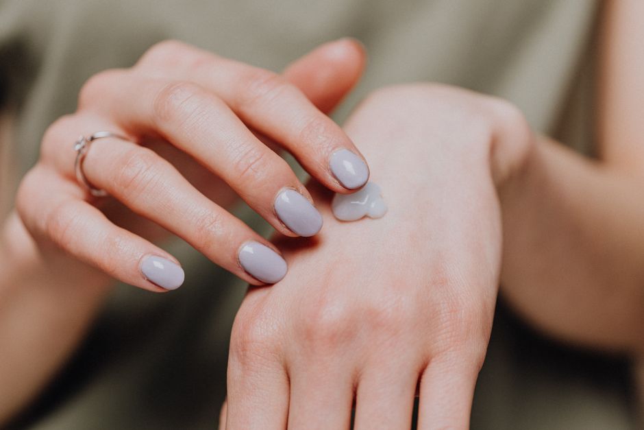 Hand with pale purple nails applying cream
