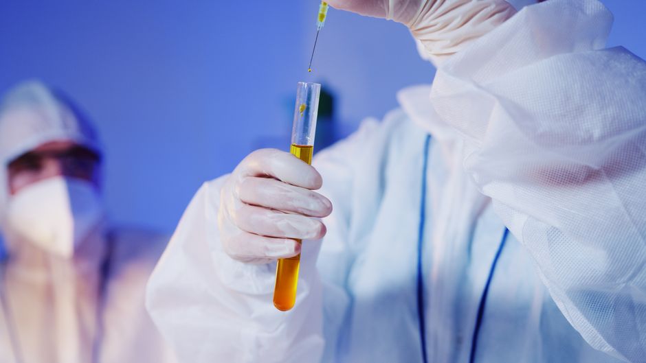 Person in protective suit holding test tube with yellow liquid