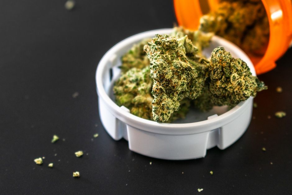 Cannabis buds in grinder with orange container