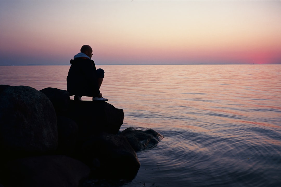 Person sitting on rocks by calm water